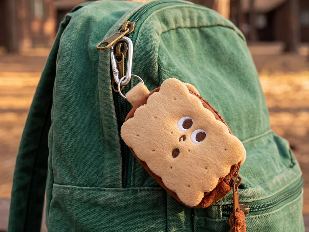 The S’mores Travel Pal clipped to the zipper of a green camp backpack in the pines